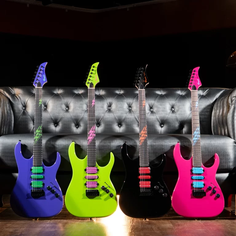 Four neon-colored electric guitars (blue, lime green, black, and pink) stand on a wooden floor in front of a tufted gray sofa. ขายราคาพิเศษ