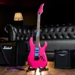 Bright pink electric guitar on a stand in a recording studio, with a Marshall amp and purple cable nearby. ขายราคาพิเศษ
