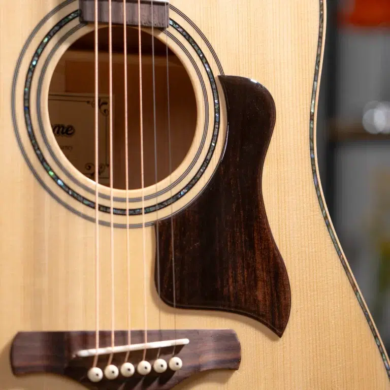 Close-up of an acoustic guitar showing the sound hole, rosette, and six strings over a light wood top. ขายราคาพิเศษ