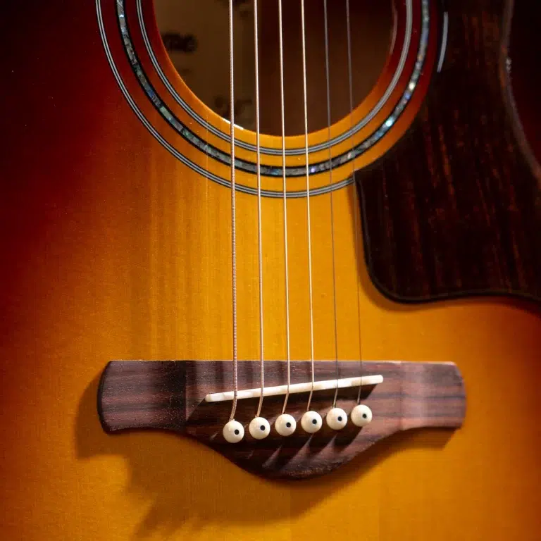 Close-up of a sunburst acoustic guitar with six strings anchored at the bridge and white pins. ขายราคาพิเศษ