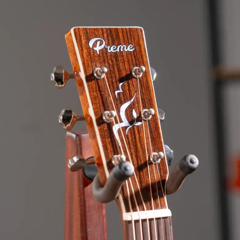 Close-up of a wooden guitar headstock on a stand, showing six tuning pegs and the brand 'Premé' with a flame logo on the headstock. ขายราคาพิเศษ