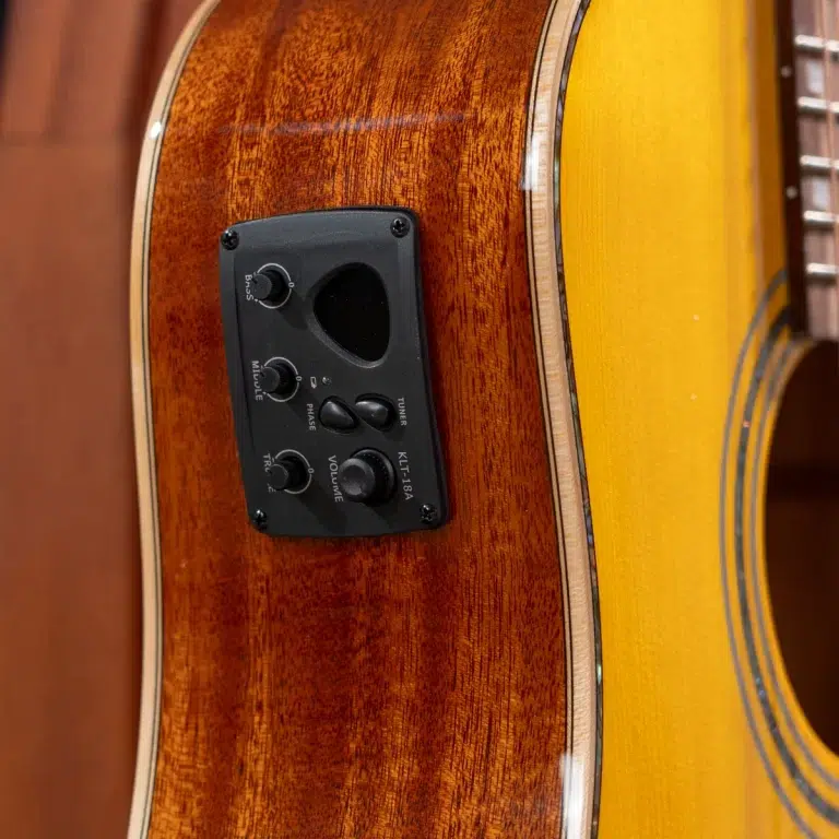 Close-up of an acoustic guitar body showing a black preamp control panel with knobs for volume, bass/treble, and phase on a rich wood finish. ขายราคาพิเศษ