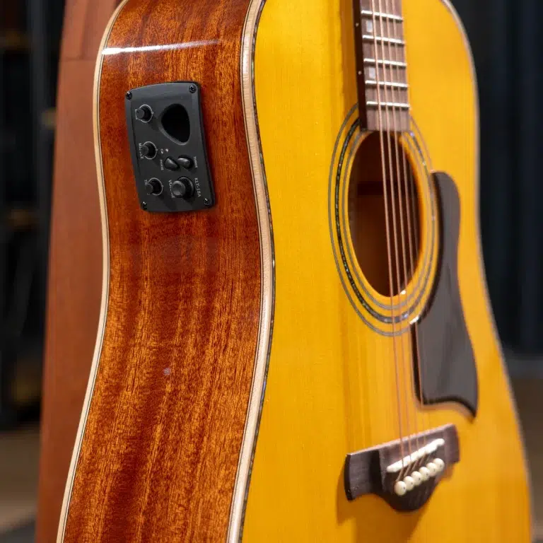 Close-up of an acoustic guitar showing yellow top, wooden back, soundhole, strings, and a side-mounted control panel (electronics). ขายราคาพิเศษ