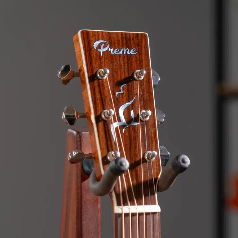 Close-up of a wooden guitar headstock with six tuning pegs and brand name 'Preme' on a stand against a gray background. ขายราคาพิเศษ