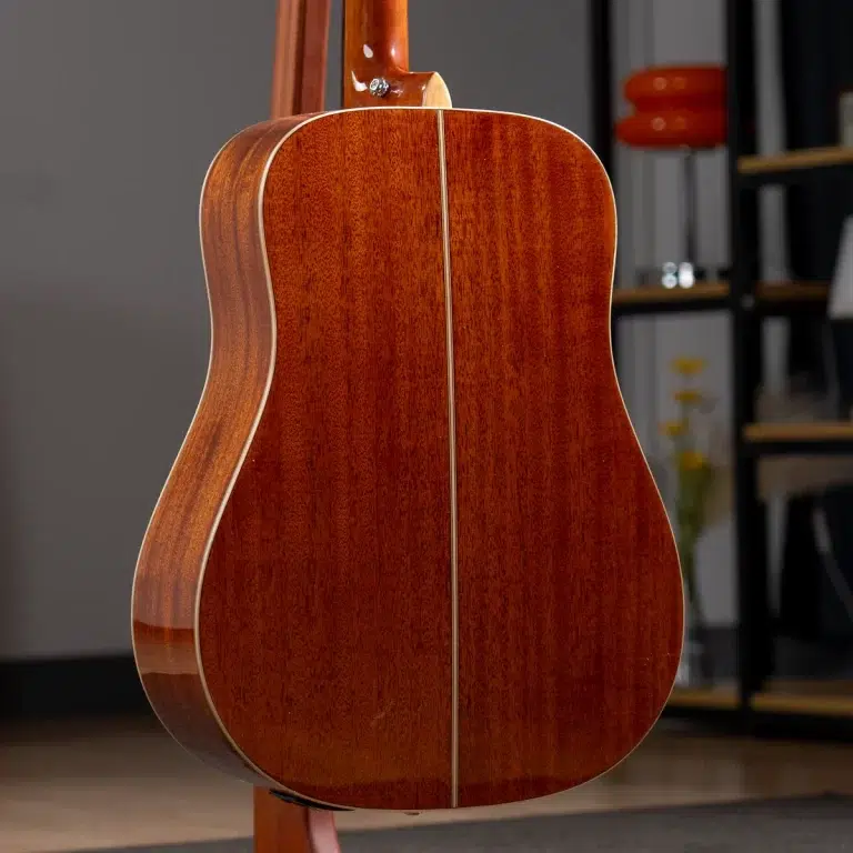 Back of a glossy brown acoustic guitar with a vertical seam, on a stand in a studio/ showroom. ขายราคาพิเศษ