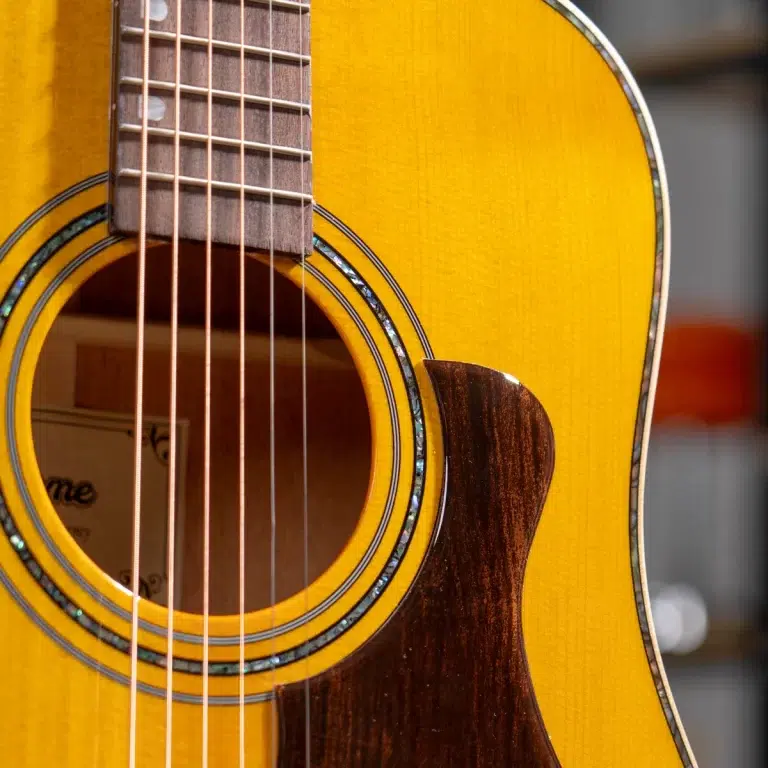 Close-up of a bright yellow acoustic guitar, showing the sound hole, decorative rosette, steel strings, and a dark wood pickguard. ขายราคาพิเศษ
