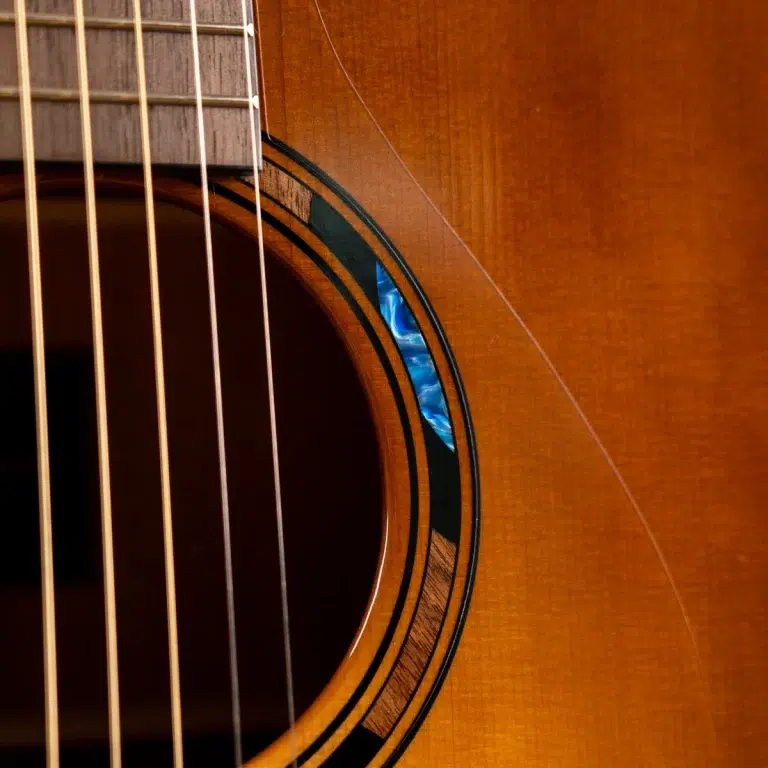 Close-up of an acoustic guitar's soundhole, strings, and warm wood grain close to the rosette. ขายราคาพิเศษ