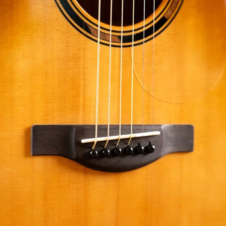 Close-up of an acoustic guitar bridge with six strings and a white saddle on a warm wood body. ขายราคาพิเศษ