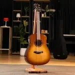 Yamaha acoustic guitar with sunburst finish on a wooden stand in a studio showroom, with shelves and a piano in the background. ขายราคาพิเศษ