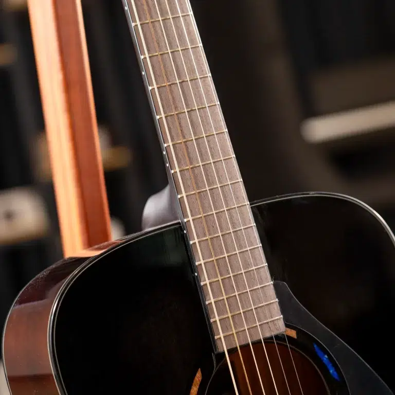 Close-up of an acoustic guitar neck and dark body, showing frets and strings against a blurred background ขายราคาพิเศษ