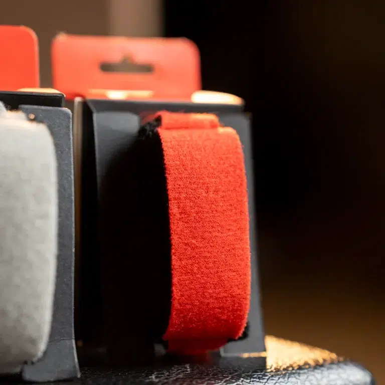 Close-up of a red fabric strap (Velcro-like texture) mounted in a black display or case. ขายราคาพิเศษ