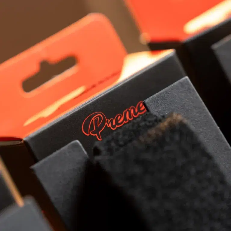 Close-up of a dark box with red 'Premier' logo, orange packaging in the blurred background. ขายราคาพิเศษ