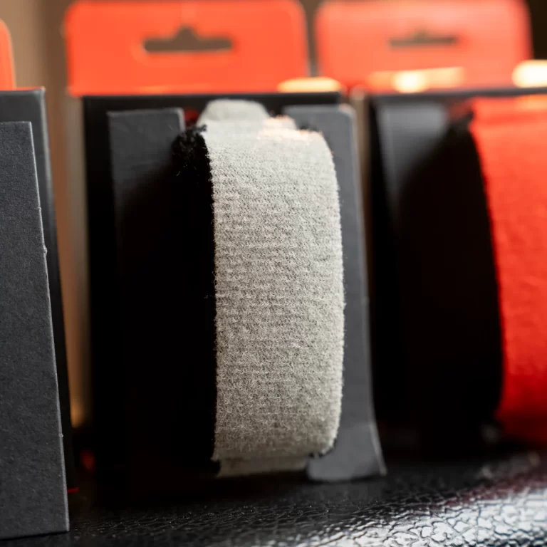 Close-up of gray fabric tape wrapped around a black spool, with red tape dispensers blurred in the background ขายราคาพิเศษ
