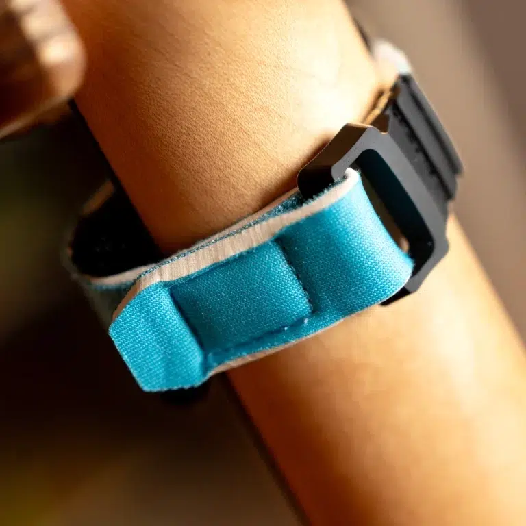Close-up of a blue fabric watch strap fastened with a black plastic buckle on a wrist. ขายราคาพิเศษ