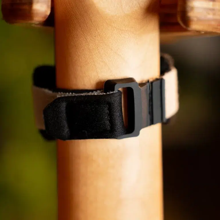 Close-up of a black nylon strap with a gray plastic buckle wrapped around a wooden post. ขายราคาพิเศษ