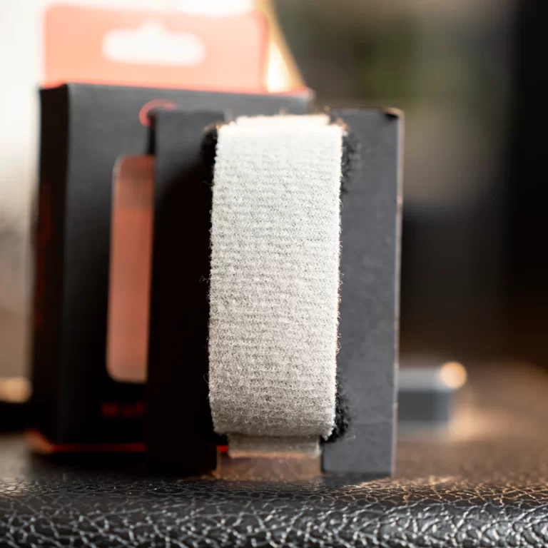 Close-up of a light gray Velcro strap wrapped around a black gadget on a textured surface. ขายราคาพิเศษ