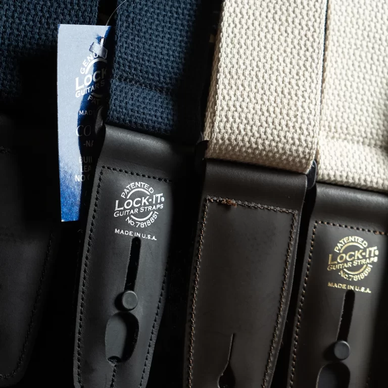Close-up of black leather guitar strap ends with a blue Lock-It tag reading 'Lock-It Guitar Straps' and 'Made in U.S.A.' ขายราคาพิเศษ