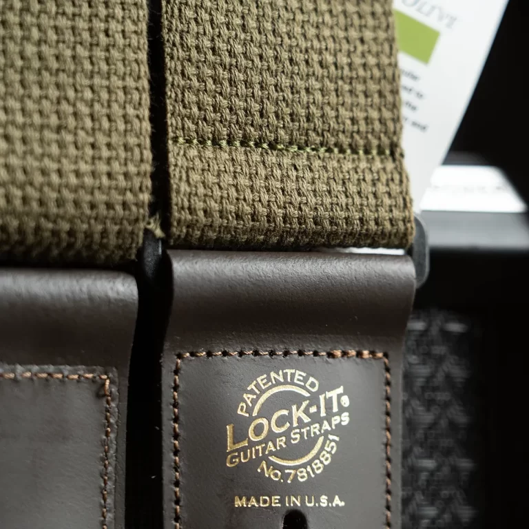 Close-up of an olive-green woven guitar strap with brown leather end, gold embossed 'LOCK-IT Guitar Straps' and 'Made in USA' text. ขายราคาพิเศษ