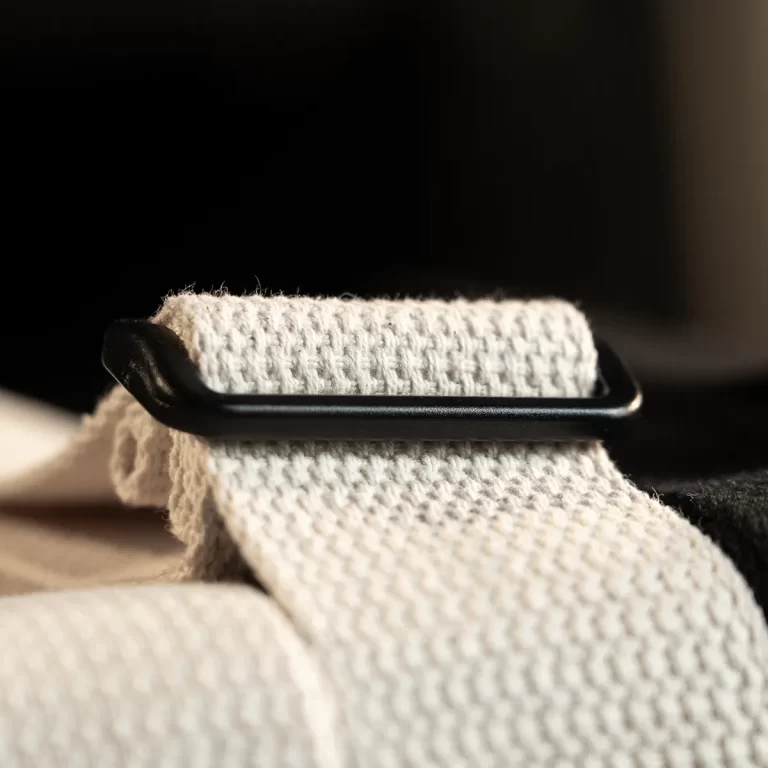 Close-up of a black strap slider resting on folded white knitted fabric, showing the adjustment bar across the material. ขายราคาพิเศษ