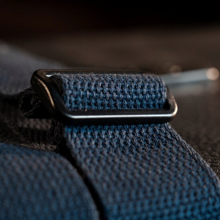 Close-up of a blue woven strap with a black metal buckle sliding along it, on a dark fabric surface. ขายราคาพิเศษ