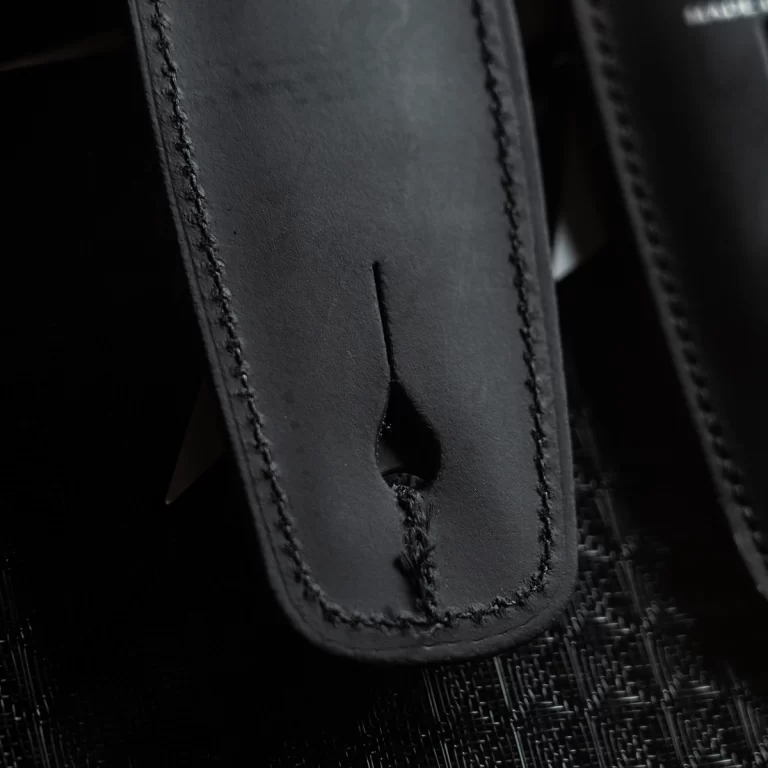 Close-up of black leather with tight stitching and a teardrop-shaped slot cutout in the center. ขายราคาพิเศษ