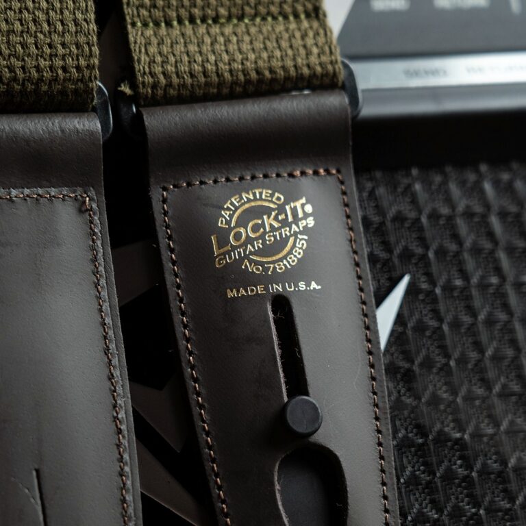 Close-up of a brown leather guitar strap with gold embossed logo: "PATENTED LOCK-IT GUITAR STRAPS Made in USA." ขายราคาพิเศษ