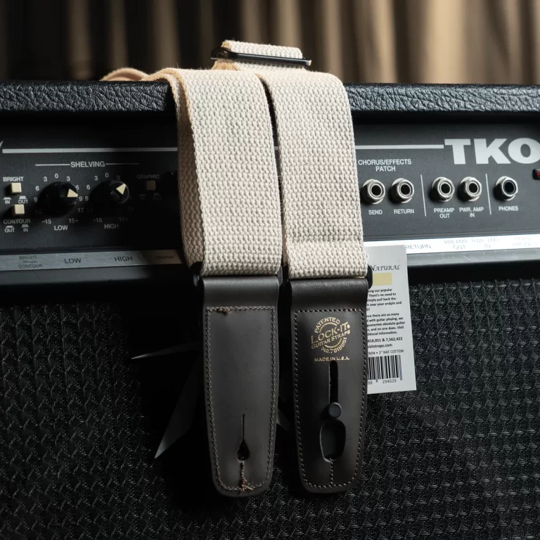 Two beige fabric guitar straps with brown leather ends draped over a black guitar amplifier head, showing the strap buckles and texture. ขายราคาพิเศษ