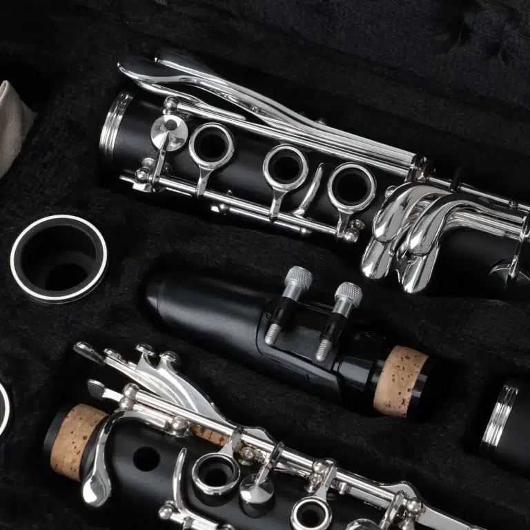 Close-up of a disassembled clarinet showing silver keys, black body, cork joints and mouthpiece parts on a dark surface ขายราคาพิเศษ