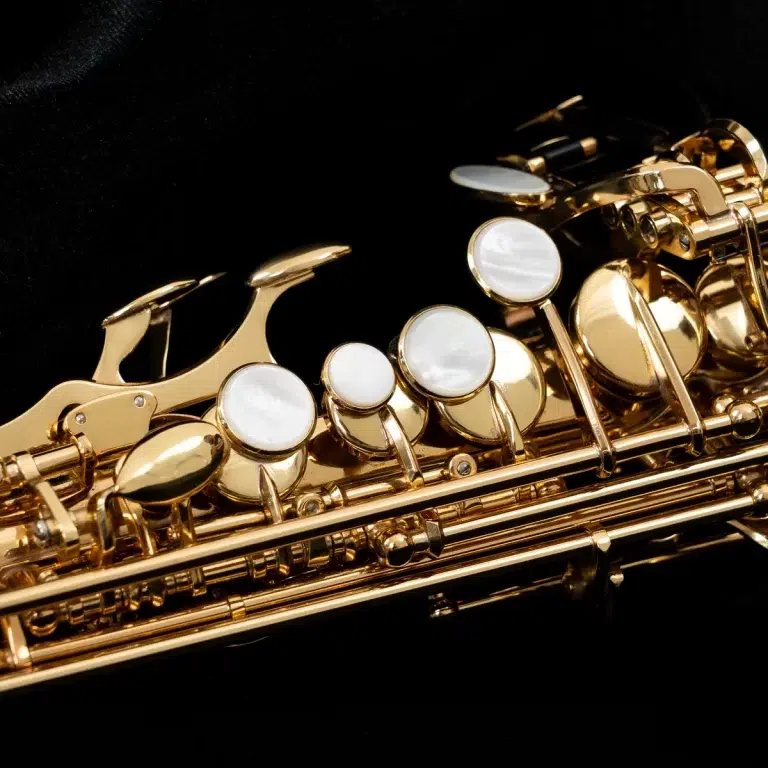 Close-up of a gold saxophone showing shiny keys and pearl-like pads against a black background. ขายราคาพิเศษ