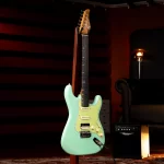 Mint green electric guitar on a stand in a dim recording studio. Plugged in with a cable visible near the floor. ขายราคาพิเศษ