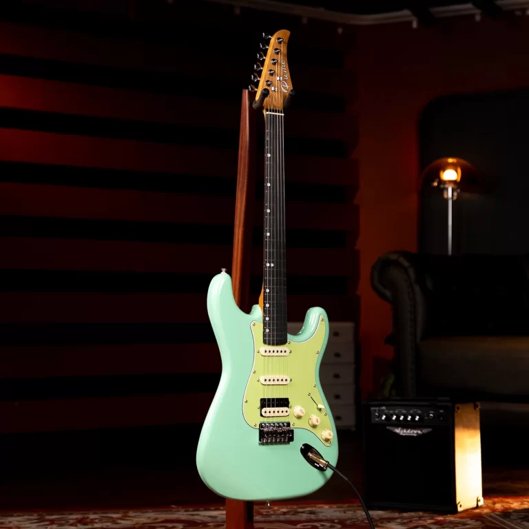 Mint green electric guitar on a stand in a dim recording studio. Plugged in with a cable visible near the floor. ขายราคาพิเศษ