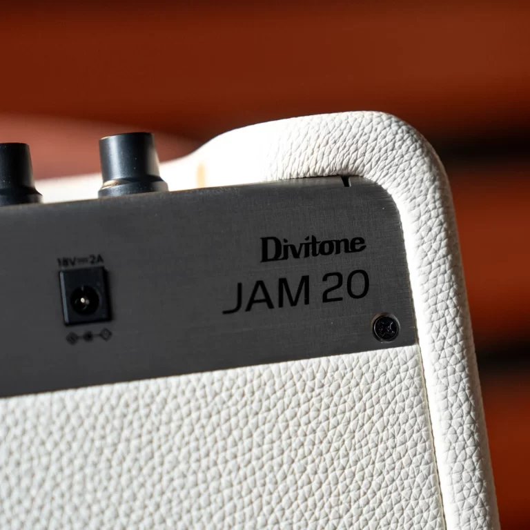 Close-up of a Divitone JAM 20 guitar amplifier top corner with a white textured cabinet and black control panel showing the power input and branding. ขายราคาพิเศษ