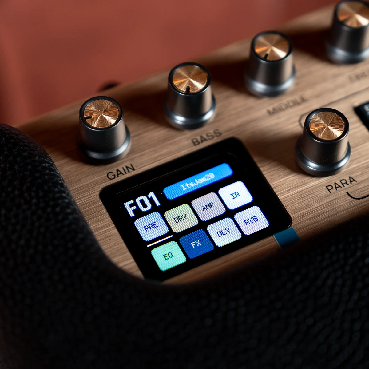 Close-up of a guitar multi-effects pedal: knobs labeled Gain, Bass, Mid, Para, and a small color LCD with labeled pads.
