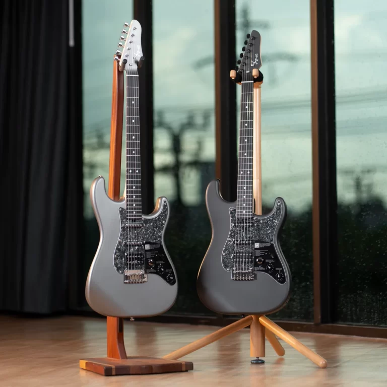 Two gray electric guitars on wooden stands indoors near large windows. ขายราคาพิเศษ