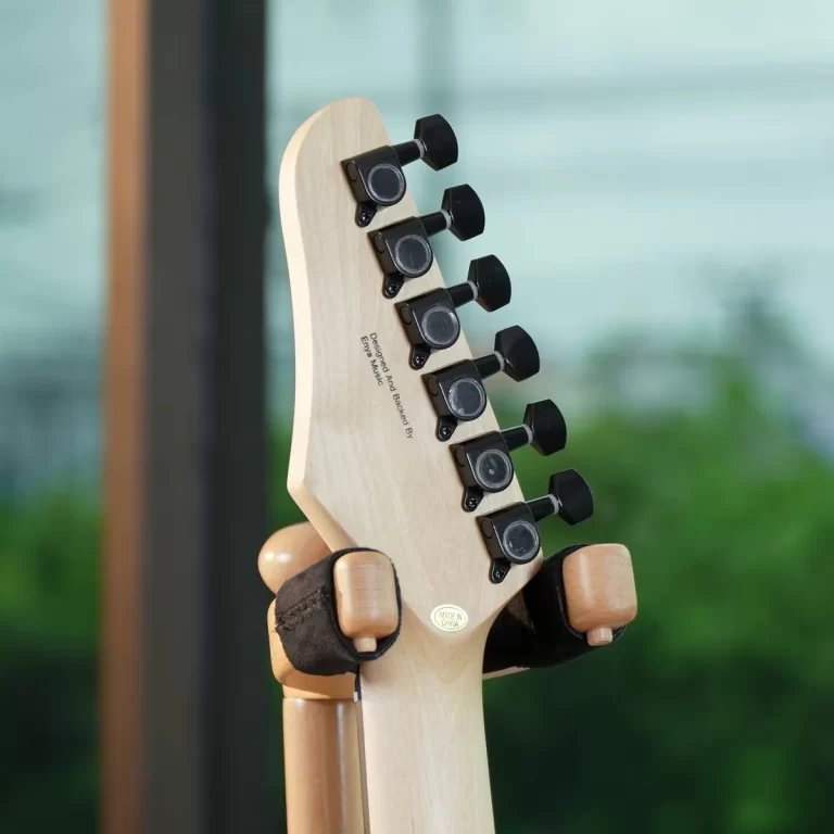 Close-up of a light wood guitar headstock with six black tuning pegs on the side, mounted in a stand. ขายราคาพิเศษ