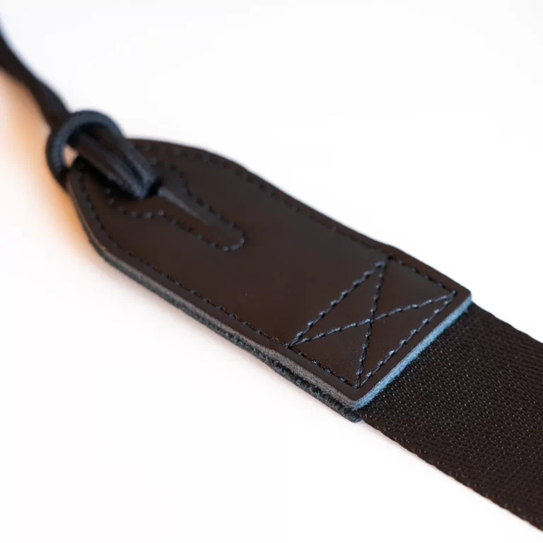 Close-up of a black leather strap tab with stitched edges attached to a black fabric strap. ขายราคาพิเศษ