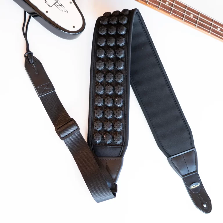 Black padded guitar strap with a studded bead pattern and leather ends, shown with a guitar nearby on a white background. ขายราคาพิเศษ