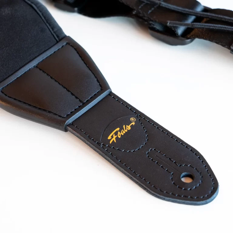 Close-up of a black strap end with stitched leather tab and a gold cursive logo, likely a bag or camera strap detail. ขายราคาพิเศษ