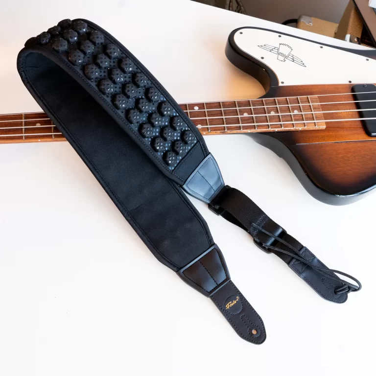 Black padded bass guitar strap with a textured surface resting on a sunburst bass guitar on a white table ขายราคาพิเศษ