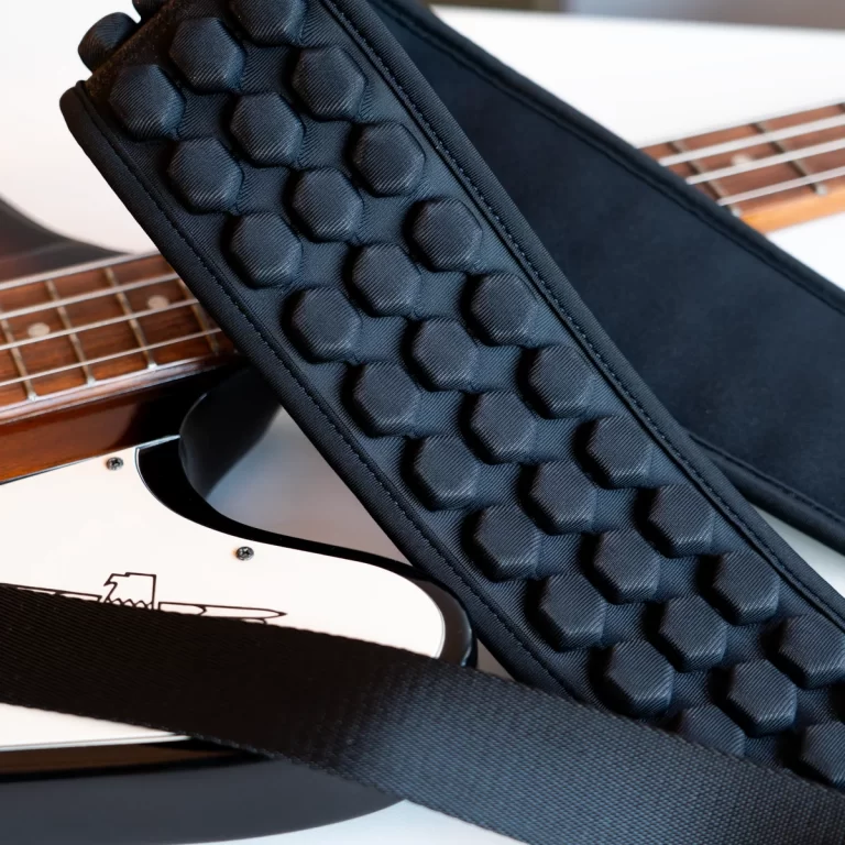 Black padded guitar strap with hexagonal pattern resting on a white electric guitar. ขายราคาพิเศษ