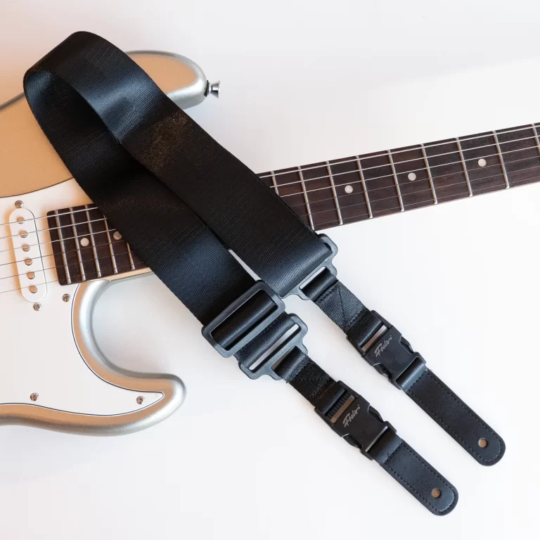 Black guitar strap laid across a silver electric guitar with a dark fretboard, resting on a white surface.