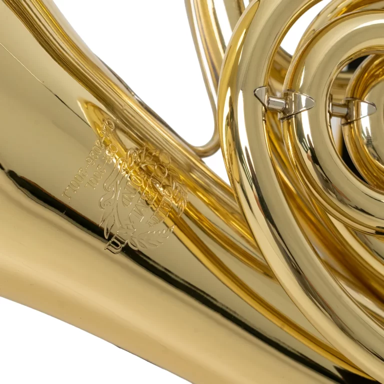 Close-up of a shiny brass French horn with coiled tubing and an engraved emblem on the bell area. ขายราคาพิเศษ