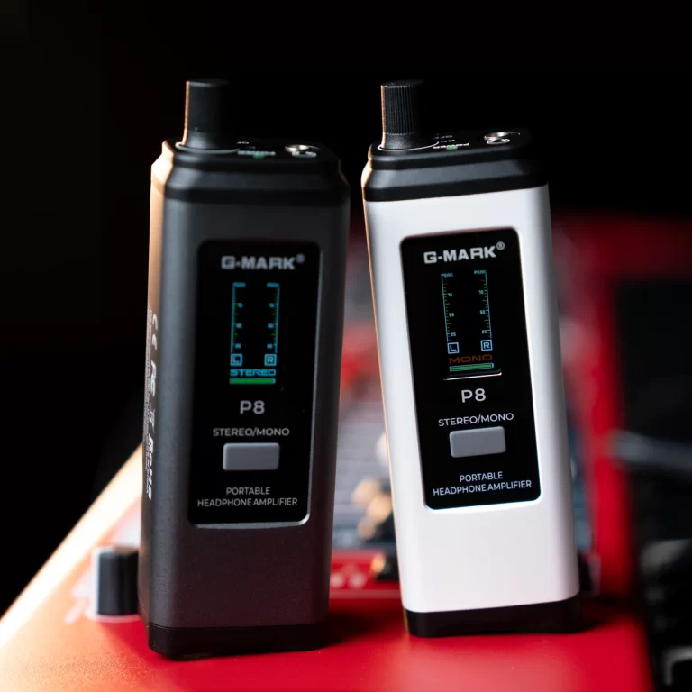 Two G-MARK P8 portable headphone amplifiers, one black and one white, standing upright on a red surface with a dark background. ขายราคาพิเศษ