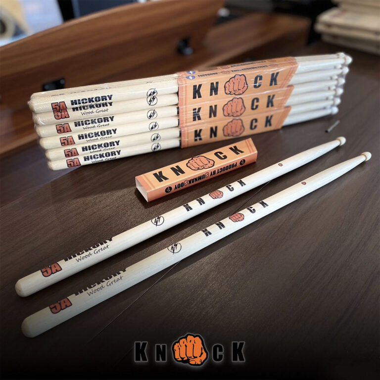 Stack of Hickory 5A drumsticks branded 'KNOCK' with an orange fist logo, laid on a wooden table. ขายราคาพิเศษ