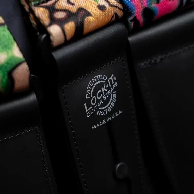 Close-up of a black leather guitar strap end with a colorful patterned strap, showing a 'Patented LOCK-IT Guitar Straps' label. ขายราคาพิเศษ