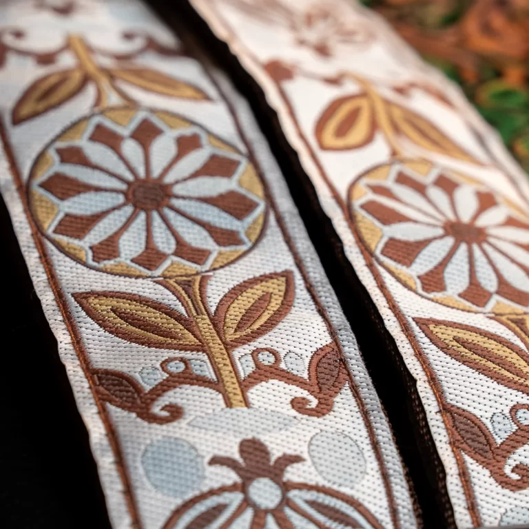 Close-up of decorative embroidered fabric trim with a brown and tan floral motif on a light background. ขายราคาพิเศษ