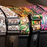 Close-up of three colorful patterned guitar straps with black metal buckles and brown leather ends, lying side by side. ขายราคาพิเศษ