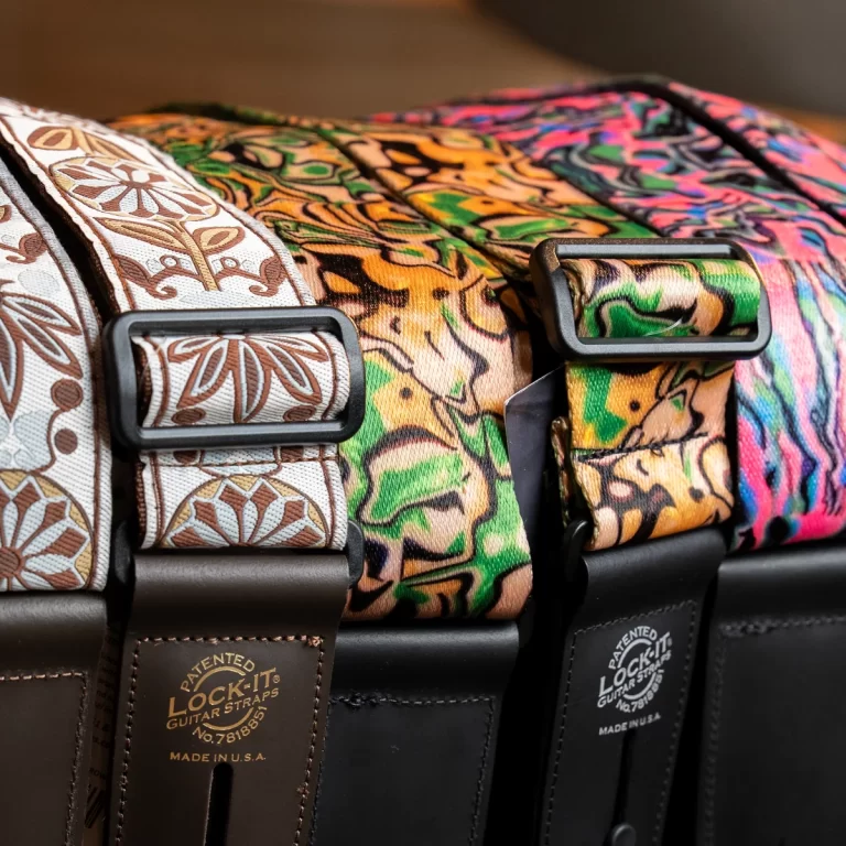 Close-up of three colorful patterned guitar straps with black metal buckles and brown leather ends, lying side by side. ขายราคาพิเศษ
