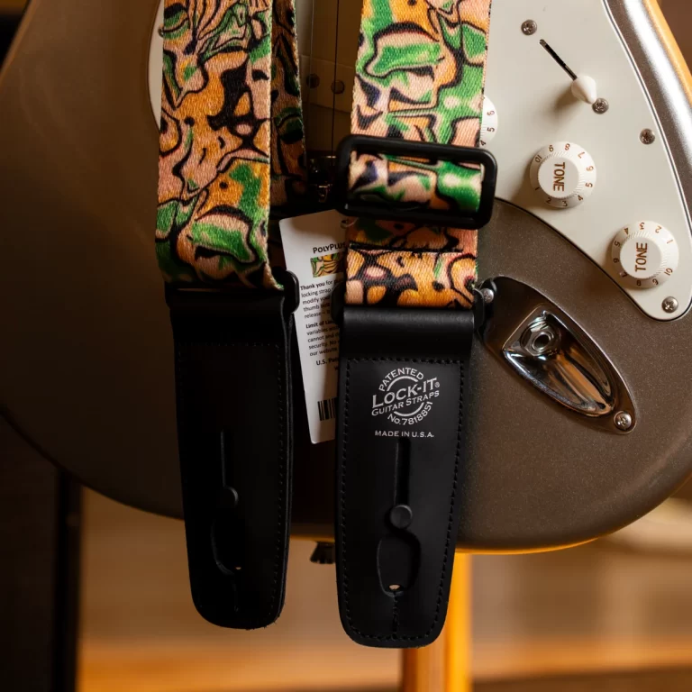 Close-up of an electric guitar with a camo-pattern strap and black leather ends, showing tone knobs on the body. ขายราคาพิเศษ