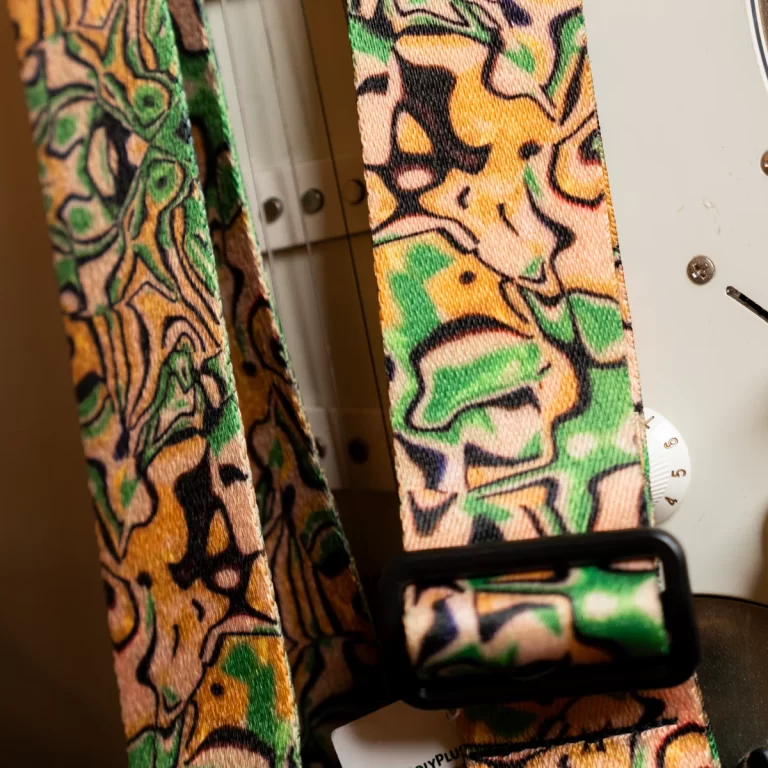 Close-up of a multicolored fabric strap with a black buckle resting against a sewing machine surface. ขายราคาพิเศษ